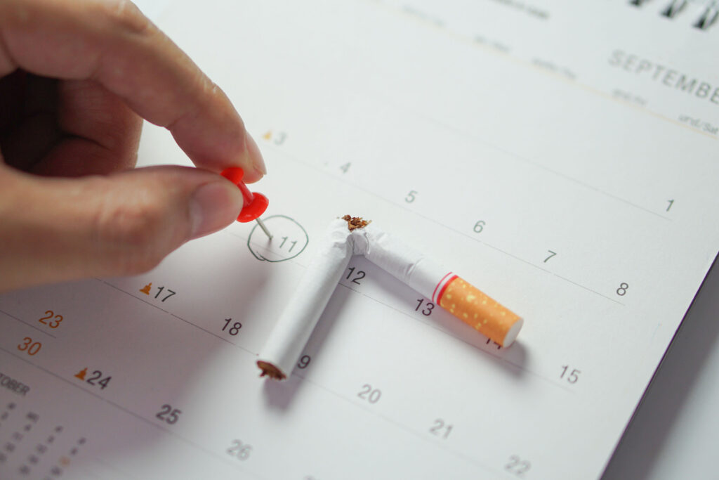 personne qui pose un pin sur une date d'un calendrier avec cigarette cassé en deux dessus signifiant qu'elle arrête le tabac aujourd'hui