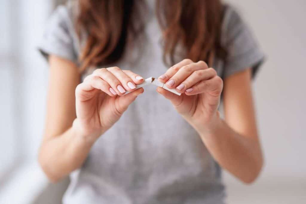 Femme au long cheveux bruns montrant son envie d'arrêter de fumer du jour au lendemain en rompant une cigarette