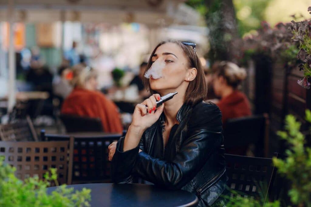 Femme en terrasse en train de fumer avec une cigarette électronique