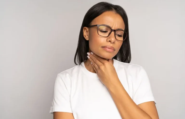 Femme touchant sa gorge avec une expression de gêne, illustrant des douleurs ou des problèmes vocaux potentiellement causés par le tabagisme.