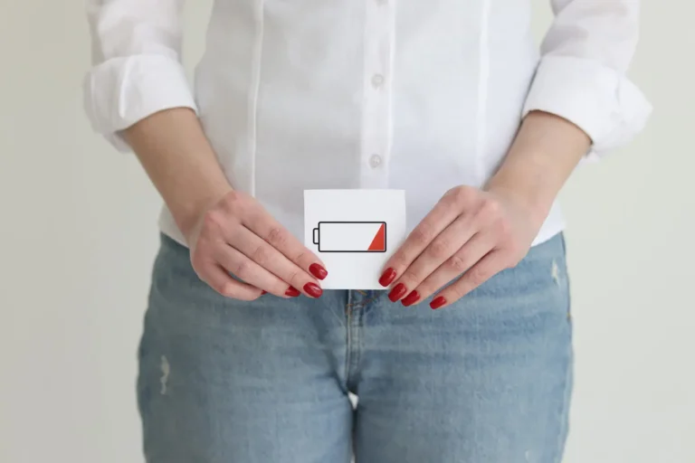 Une femme tenant une carte avec une icône de batterie faible devant son bas-ventre, symbolisant la fatigue ou une baisse d’énergie, potentiellement liée à une diminution de la libido.