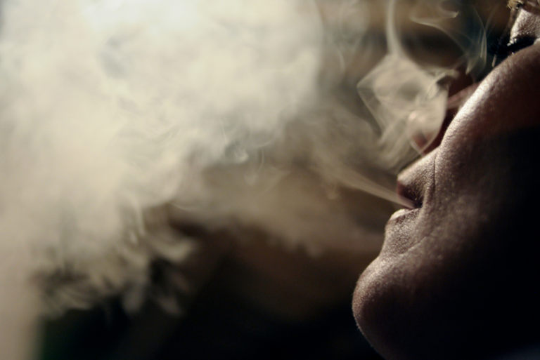 Gros plan de profil de la bouche et du menton d'une personne en train de recracher un nuage de fumée de cigarette