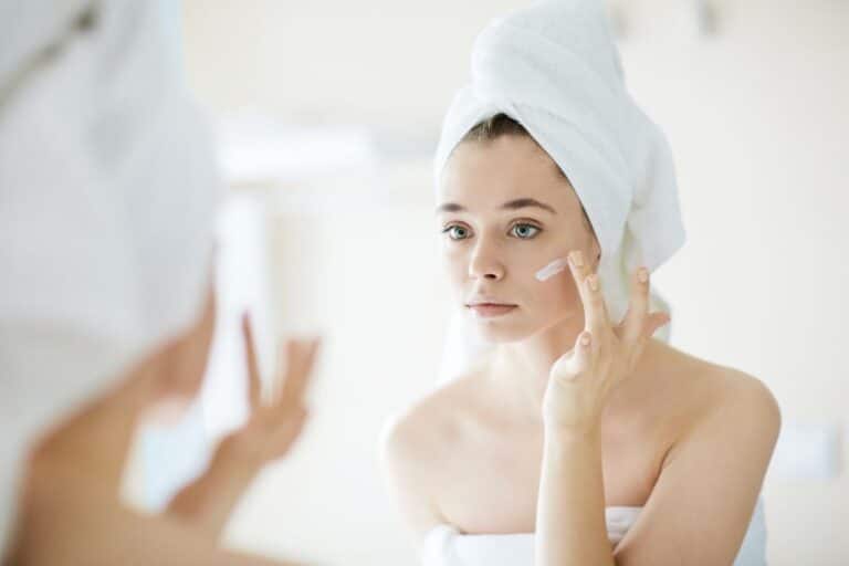 Femme sortant de la douche et appliquant une crème pour le visage devant un miroir