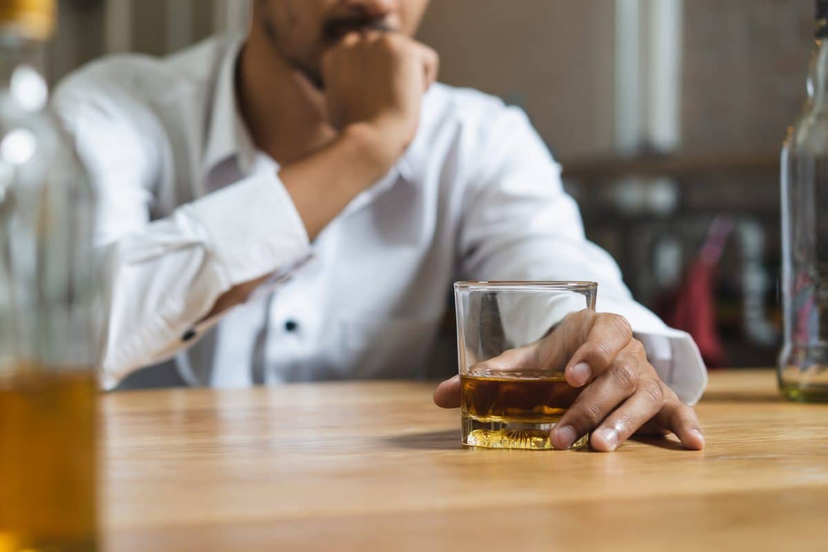 Homme accoudé à un comptoir, la main posée sur un verre de whisky