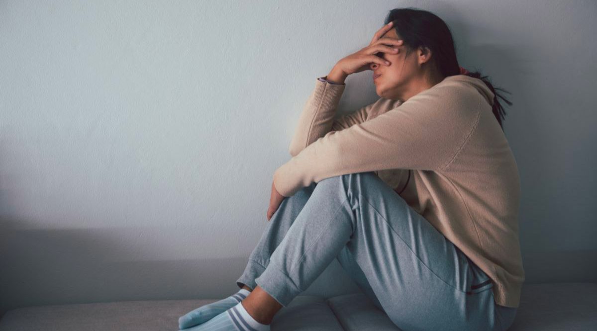 Jeune femme en dépression, assiste par terre, une main sur le visage.