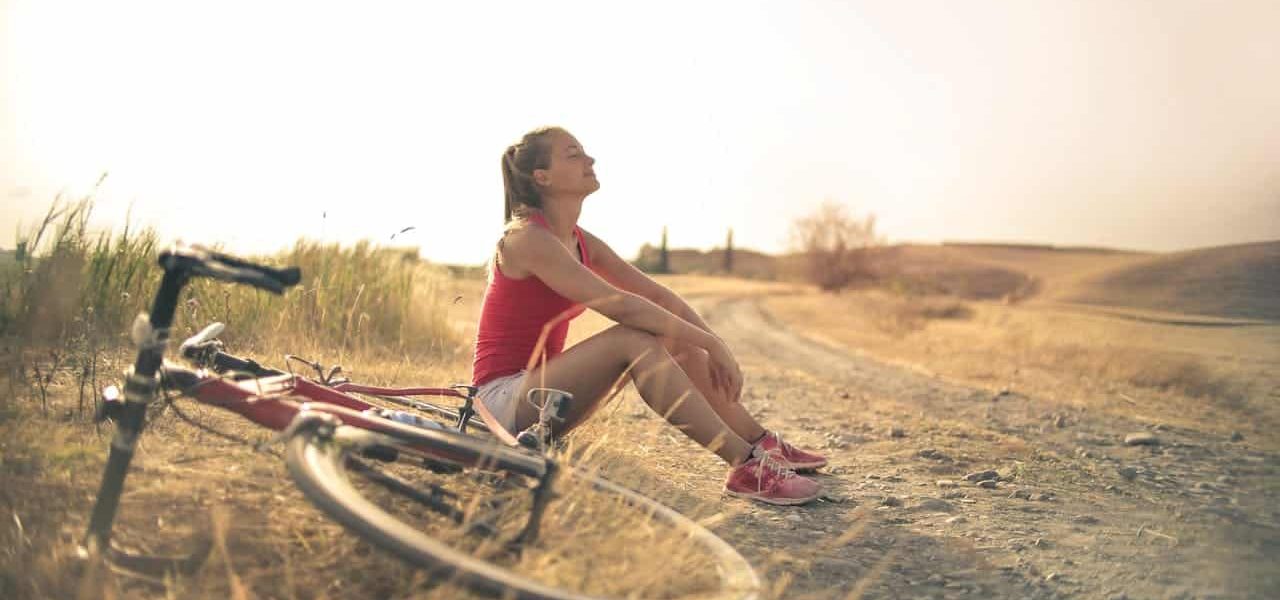 Femme sportive assise sur le sol à côté d'un vélo respirant l'air frais