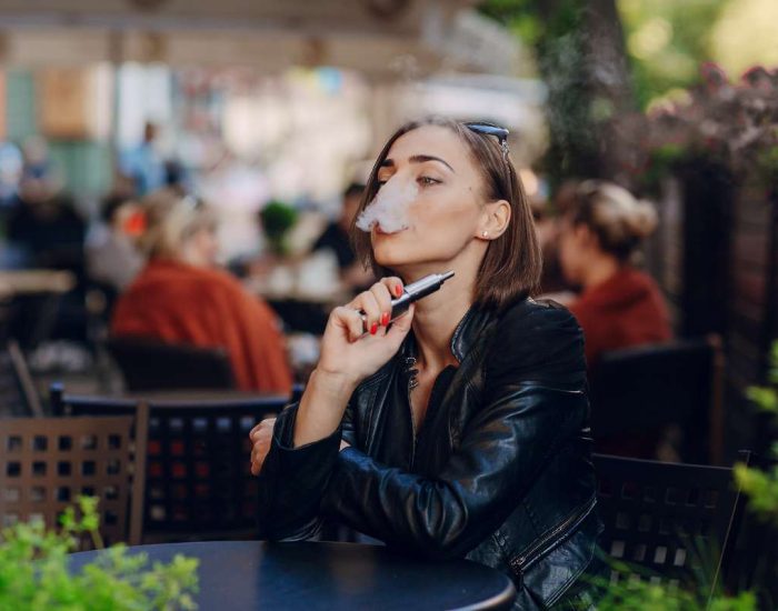 Femme en terrasse en train de fumer avec une cigarette électronique