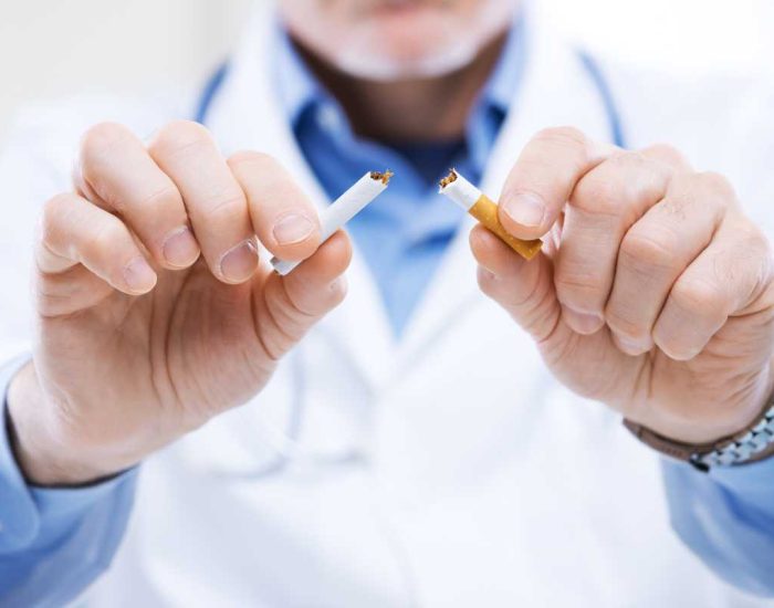 Médecin en blouse blanche en train de couper une cigarette en deux