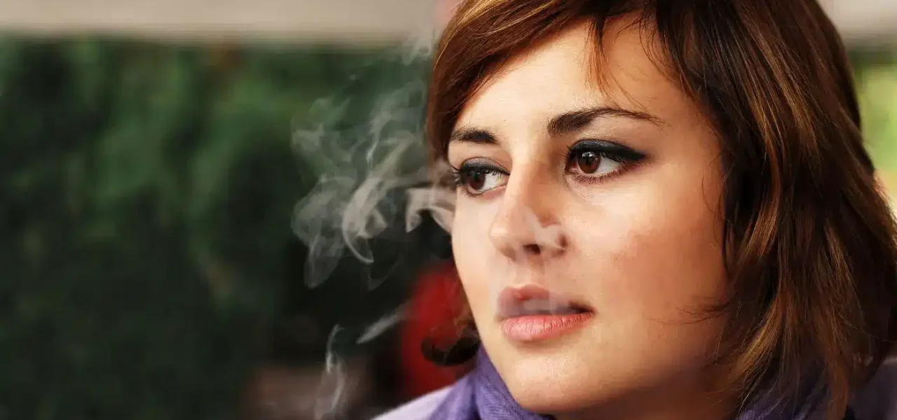 Femme fumant une cigarette, entourée de fumée, illustrant les effets nocifs du tabagisme sur la santé oculaire et générale.