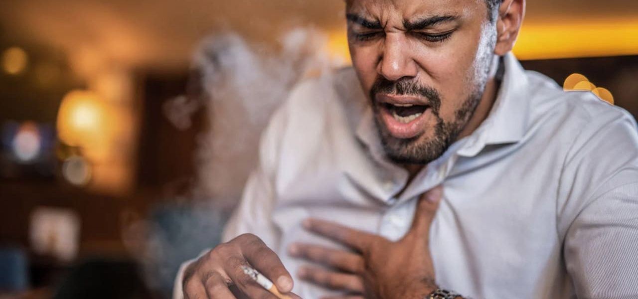 Jeune homme toussant après avoir fumé une cigarette.